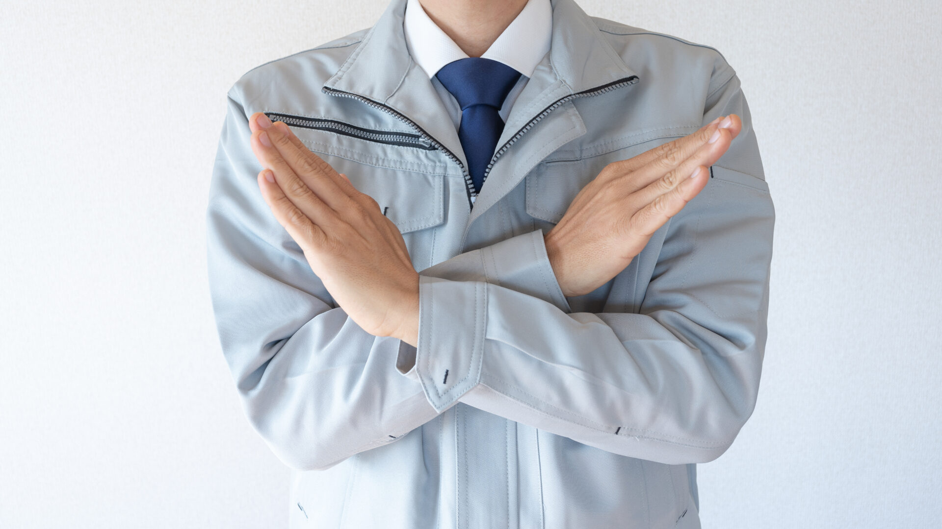 腕でバツ印をつくる作業着の男性